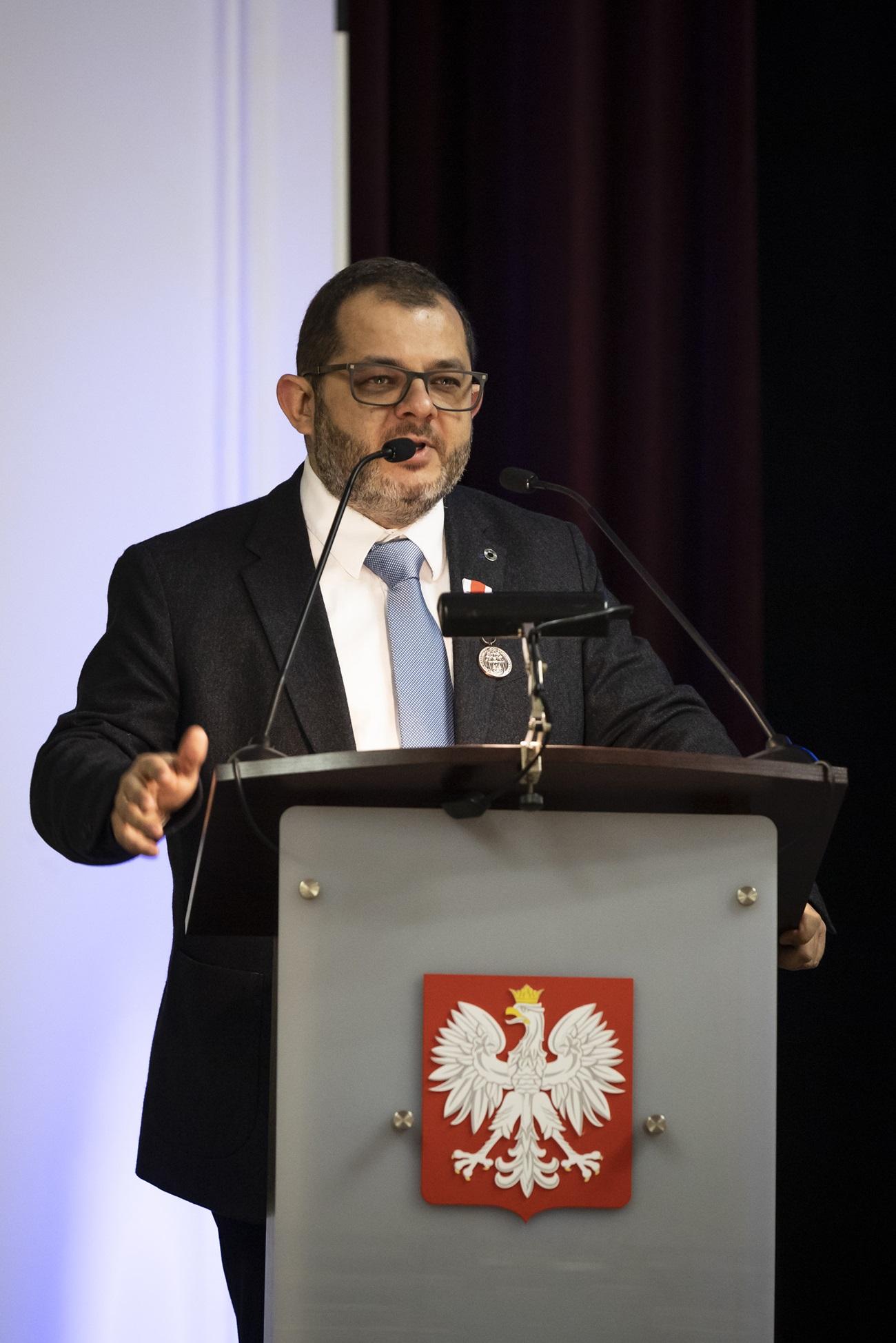 Profesor Tomasz Grzyb stojący przy mównicy. Z przodu mównicy widać logo Polski.