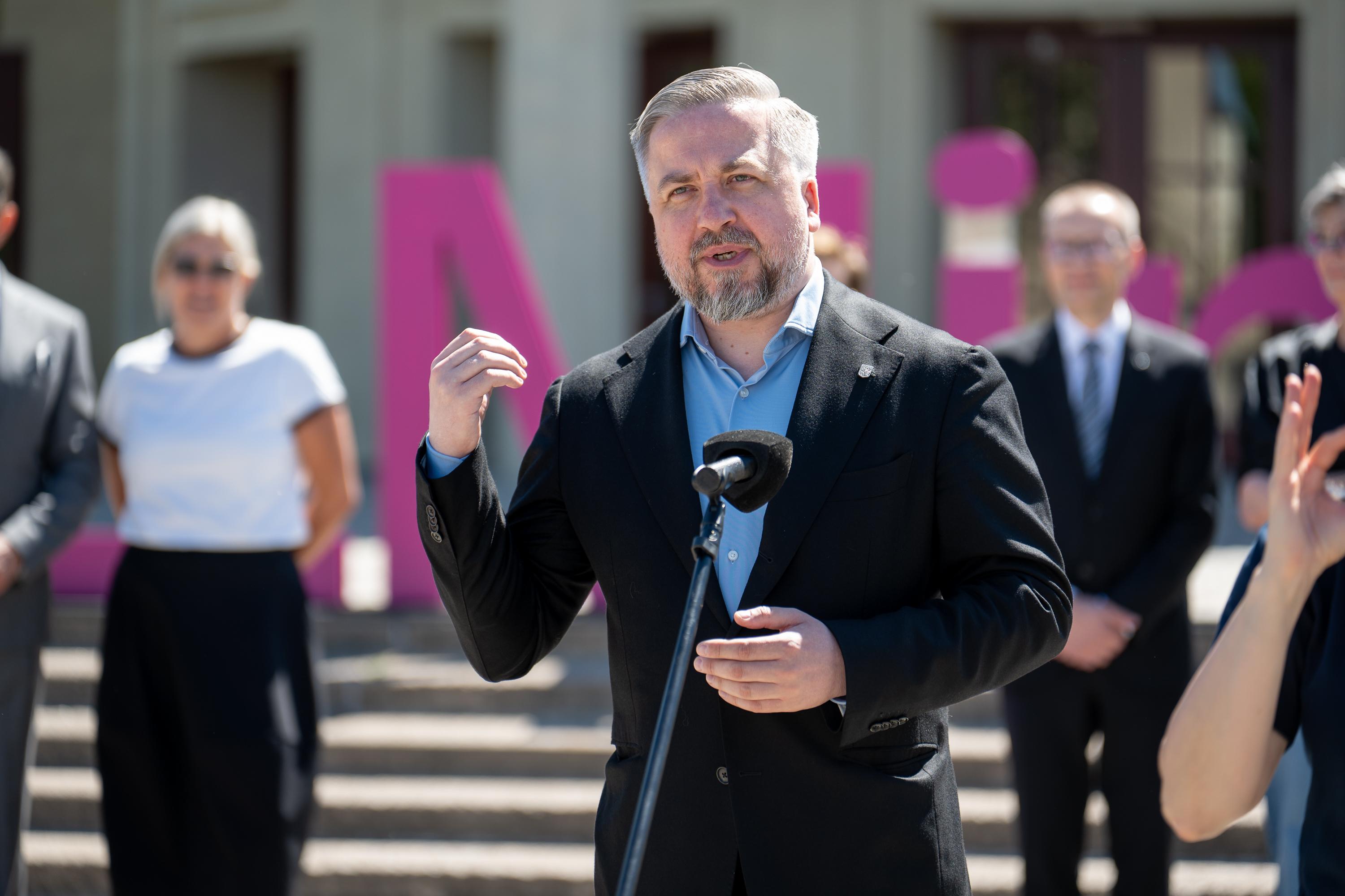 mężczyzna w garniturze przemawia do mikrofonu na placu pod Iglicą przy Hali Stulecia we Wrocławiu, w tle uczestnicy konferencji i duże litery w fioletowo-różowej kolorystyce z napisu Re_Minnd