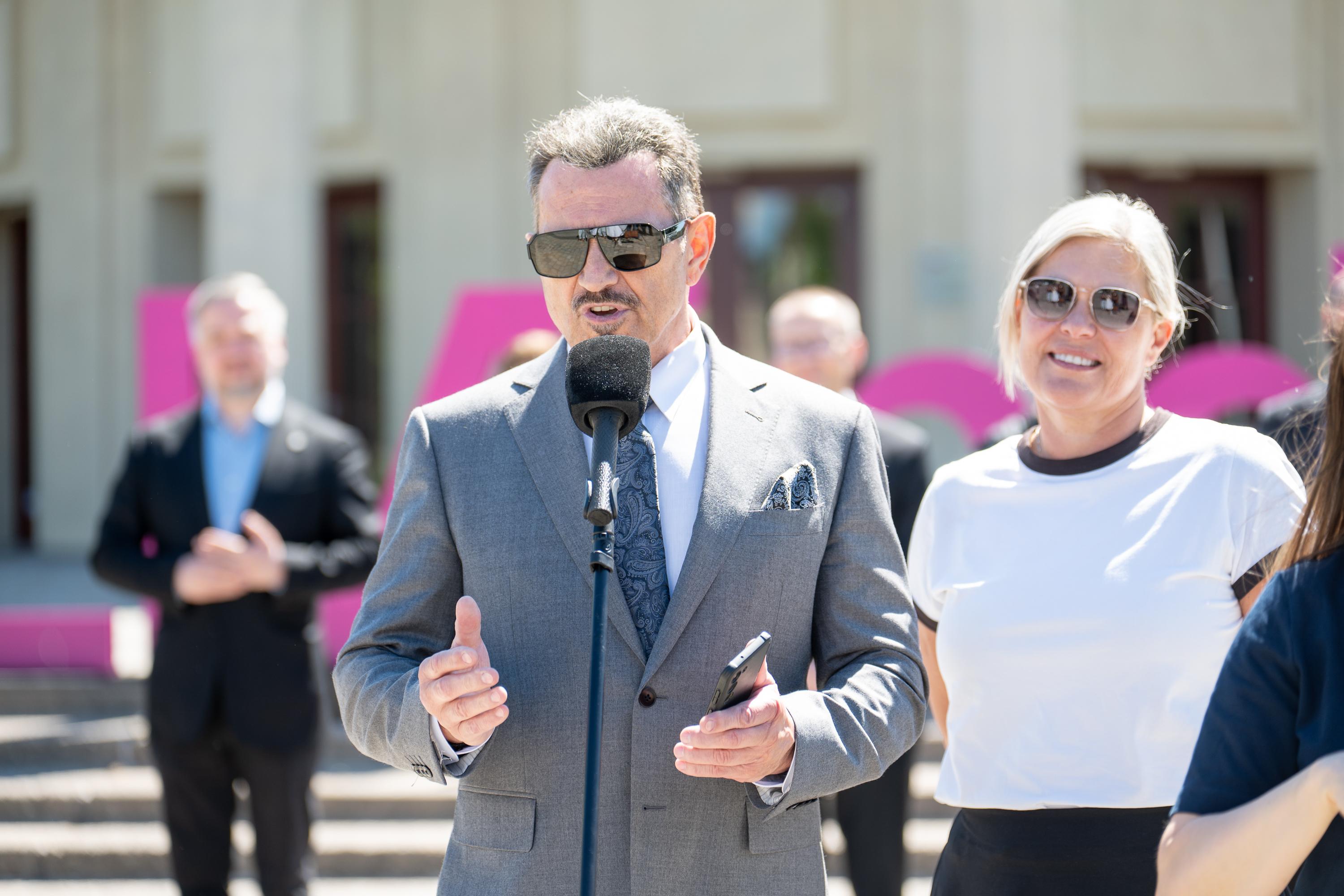 mężczyzna w garniturze przemawia do mikrofonu na placu pod Iglicą przy Hali Stulecia we Wrocławiu, w tle uczestnicy konferencji i duże litery w fioletowo-różowej kolorystyce z napisu Re_Minnd