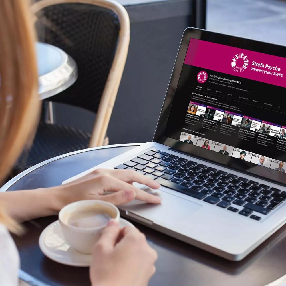 Kobieta w kawiarni ogląda na laptopie webinar Strefy Psyche Uniwersytetu SWPS