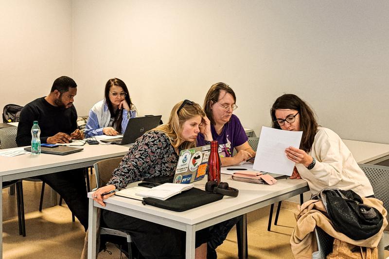 Zespoły studenckie pracują w grupach siedząc przy stołach