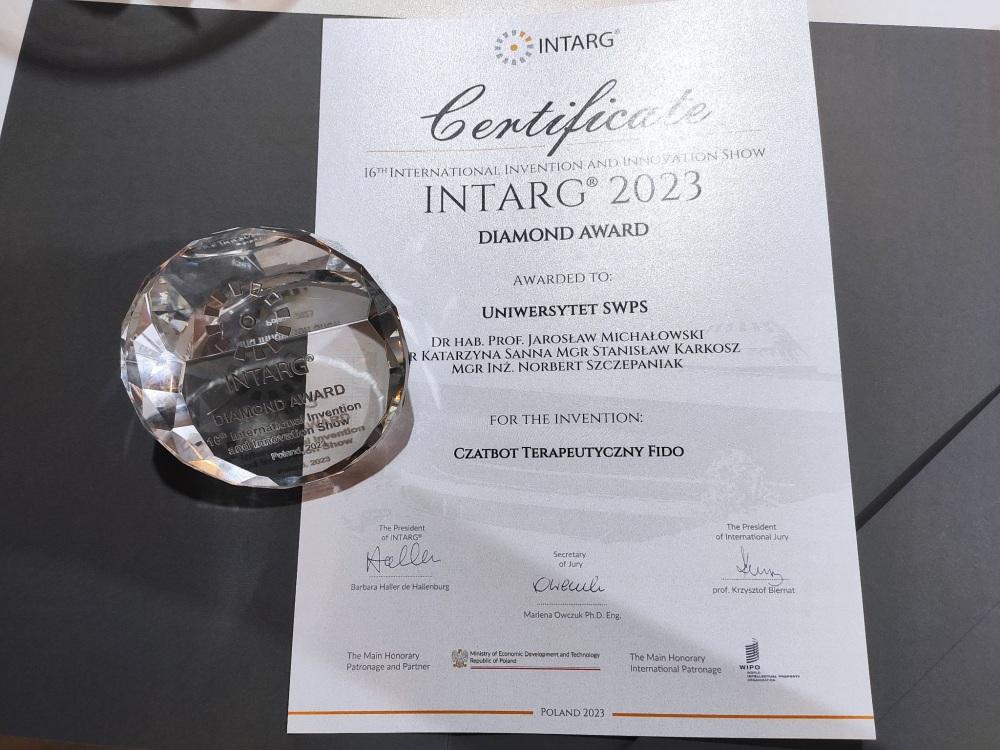 Zdjęcie certyfikatu „Diamond Award” dla Uniwersytetu SWPS za chatbota terapeutycznego Fido. Na certyfikacie leży diament z napisami