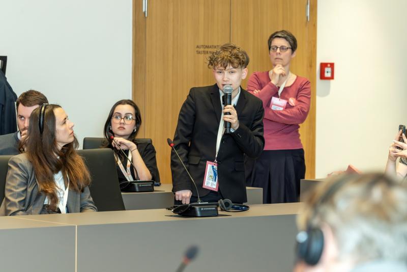 Student z kręconymi włosami zadaje pytanie podczas konferencji
