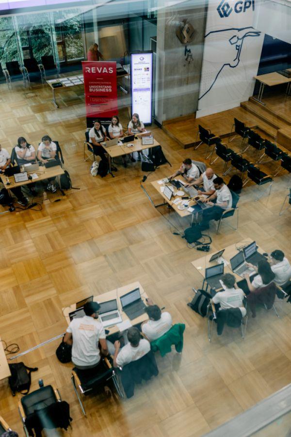 Akademickie Mistrzostwa Menedżerskie. Trzyosobowe zespoły siedzą przy osobnych biurkach z laptopami, widok z góry