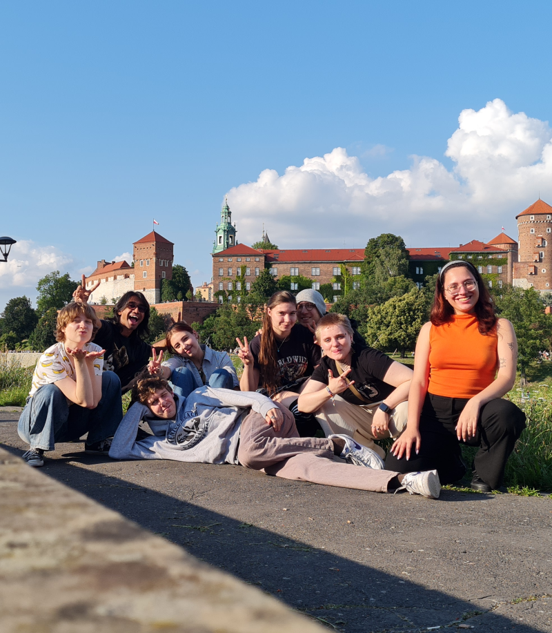 Ośmioro uśmiechniętych, rozluźnionych studentek i studentów pozuje do zdjęcia na tle Wawelu