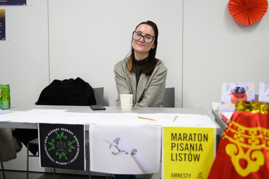 Stoisko z rozłożonymi kartkami i długopisami oraz plakatem z napisem „Maraton Pisania Listów Amnesty International”
