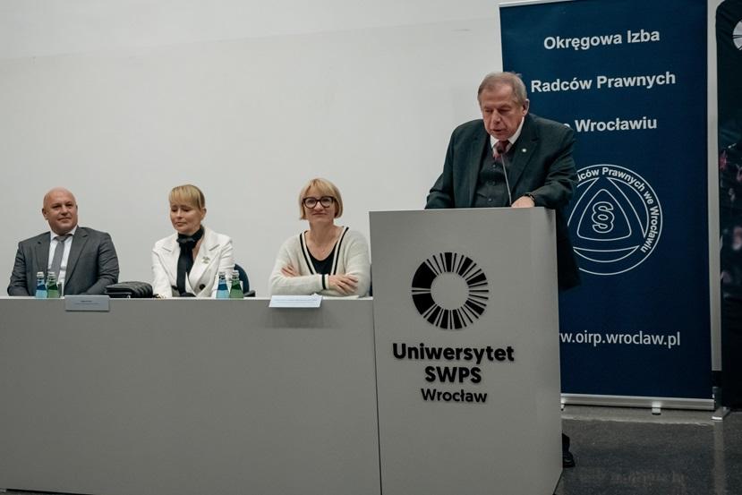 Mecenas Andrzej Malicki stojący przy mównicy obok stołu jury