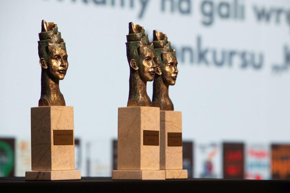 Trzy złote statuetki w kształcie twarzy z napisem „Książka dla trenera 2024”