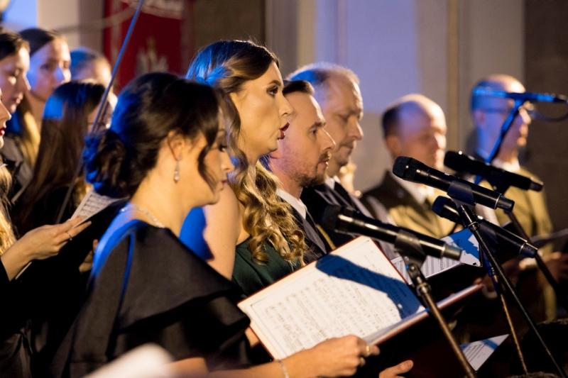 Koncert Chóru Akademickiego Uniwersytetu SWPS w Katedrze Polowej Wojska Polskiego. Zbliżenie z boku na chórzystki i chórzystów oraz mikrofony przed nimi