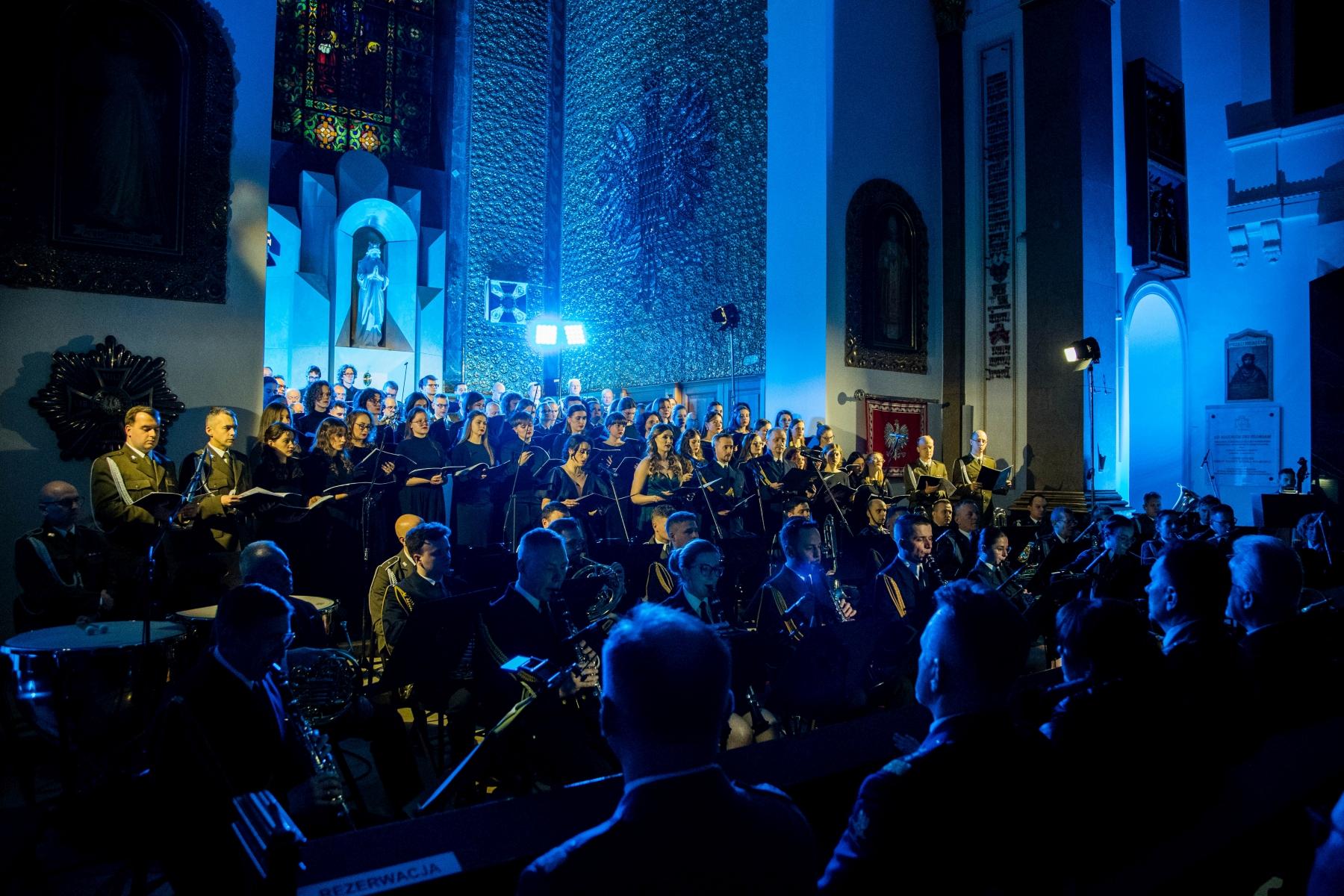 Koncert Chóru Akademickiego Uniwersytetu SWPS w Katedrze Polowej Wojska Polskiego. Chóry i orkiestra w trakcie koncertu. W tle widoczny jest ołtarz, a wnętrze oświetla nastrojowe światło