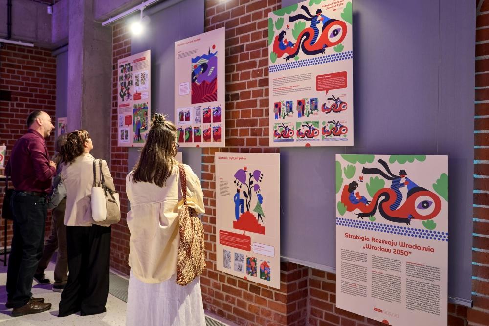 Trzy osoby oglądają plakaty z grafikami do Strategii Wrocław 2050