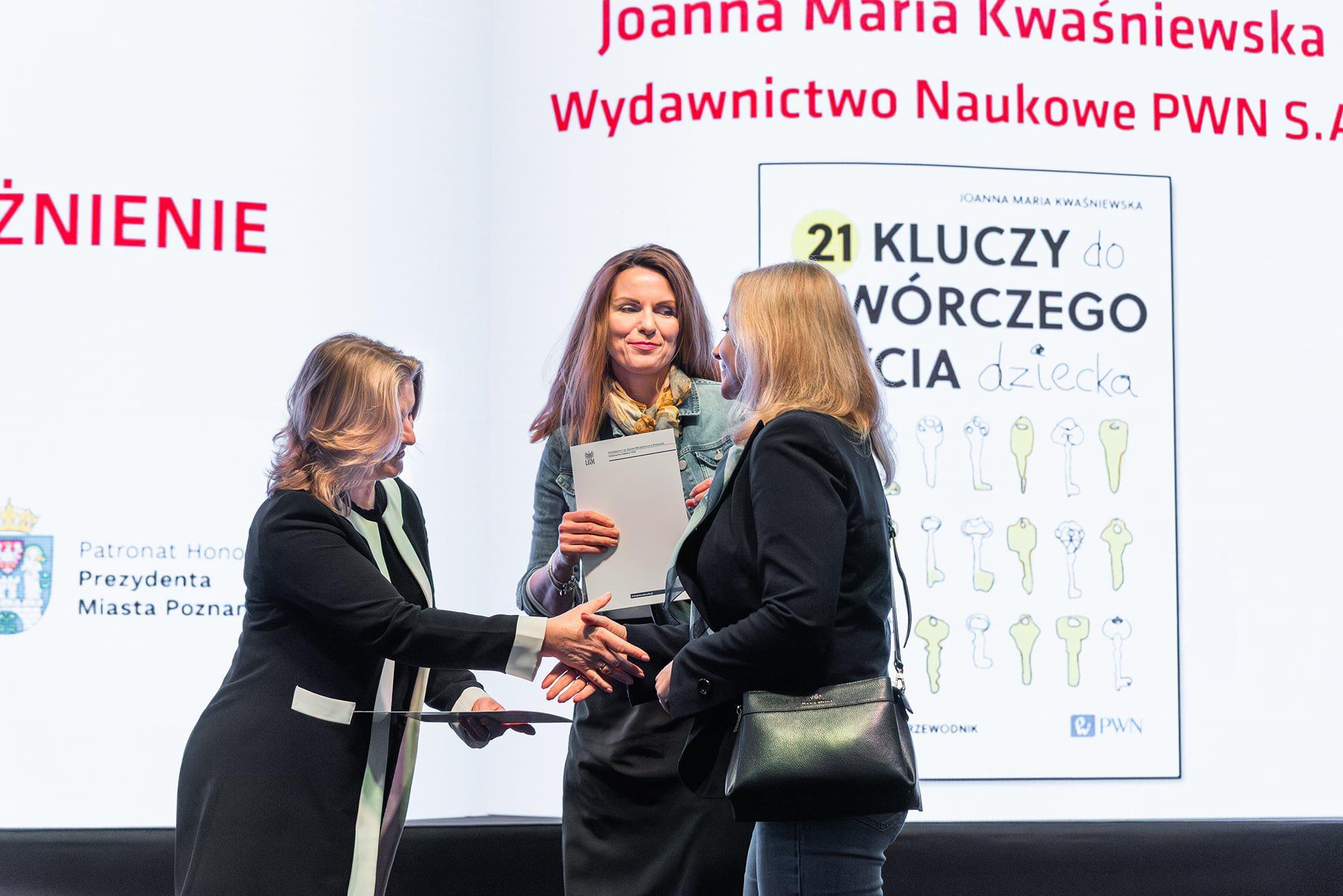 Doktor Joanna Kwaśniewska stoi na scenie z dyplomem i patrzy, jak Dorota Siudowska-Mieszkowska odbiera wyróżnienie