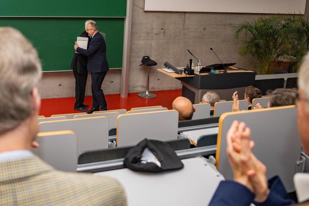 Na pierwszym planie publiczność uroczystości, na drugim planie Adam Bodnar i Andreas Zimmermann w uścisku po wręczeniu dyplomu