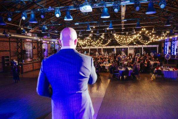 Gala Nagrody Stowarzyszenia PRom 2026. Widok zza pleców prelegenta na widownię siedzącą przy stołach na sali bankietowej